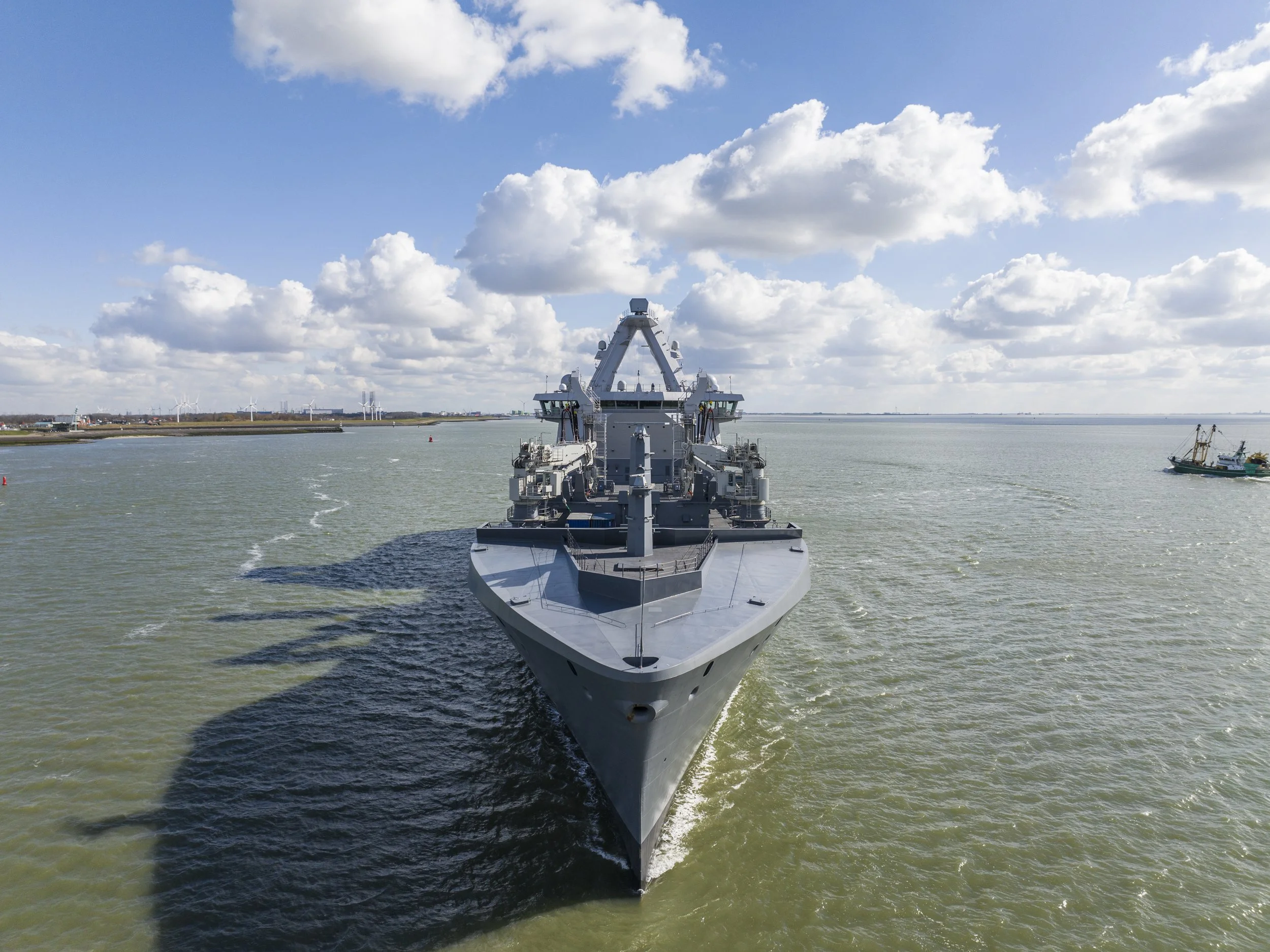 A large gray warship sailing in a body of water under a partly cloudy sky.