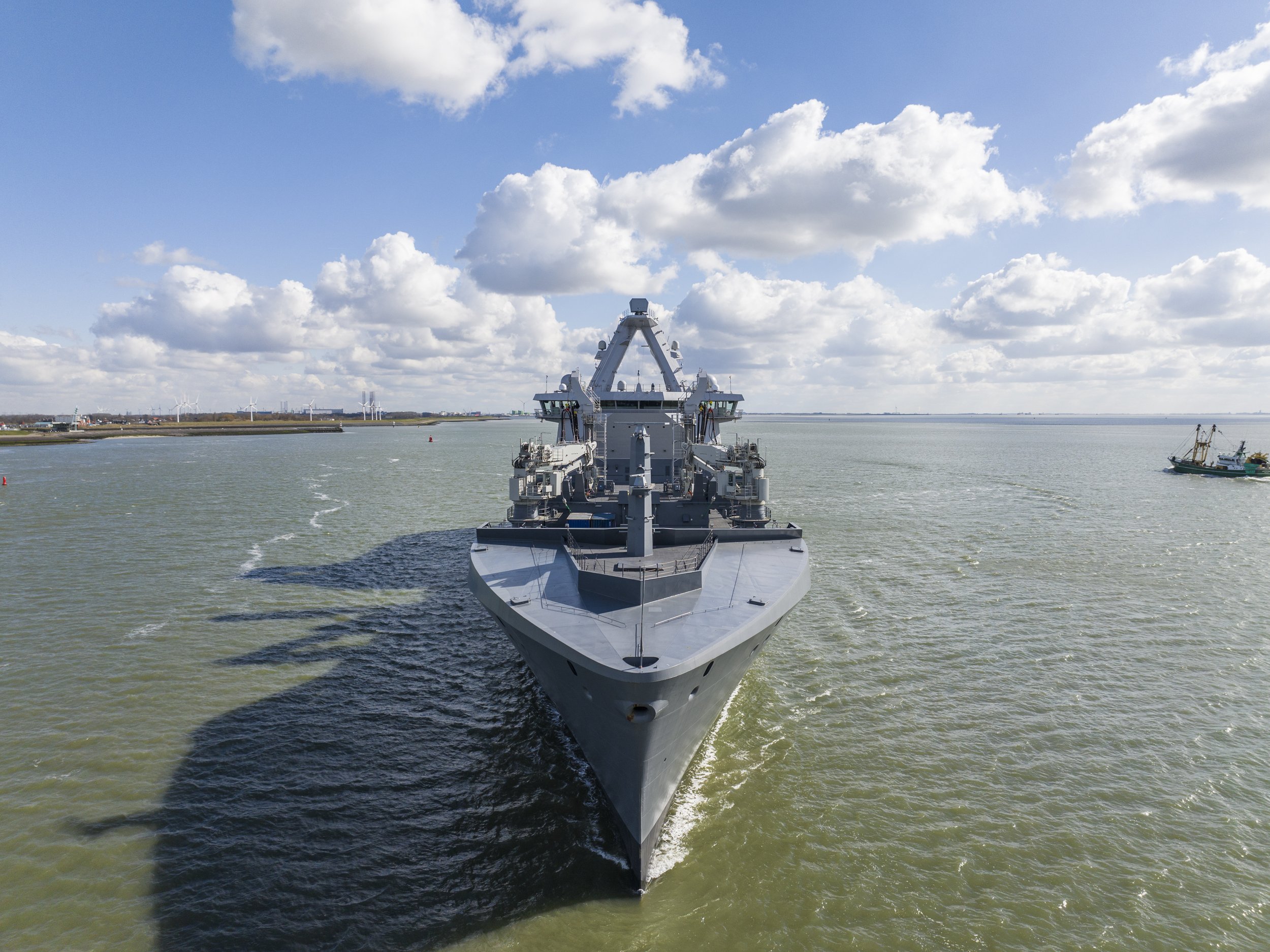 A large naval warship sailing on the water during daytime with a partly cloudy sky.