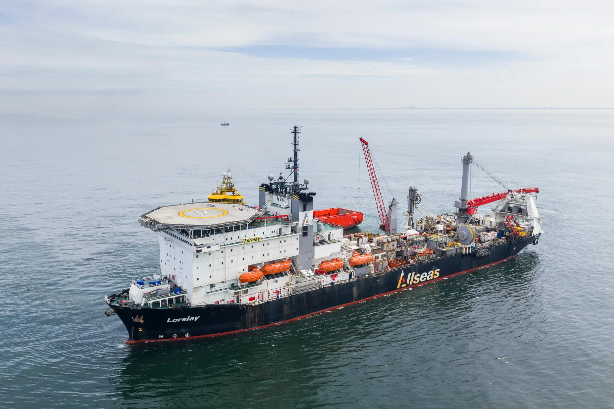 A large offshore supply vessel named Lorelay with a helipad on the deck, floating on calm water. The ship has various equipment, cranes, and lifeboats. The background shows an open sea with a distant small boat.