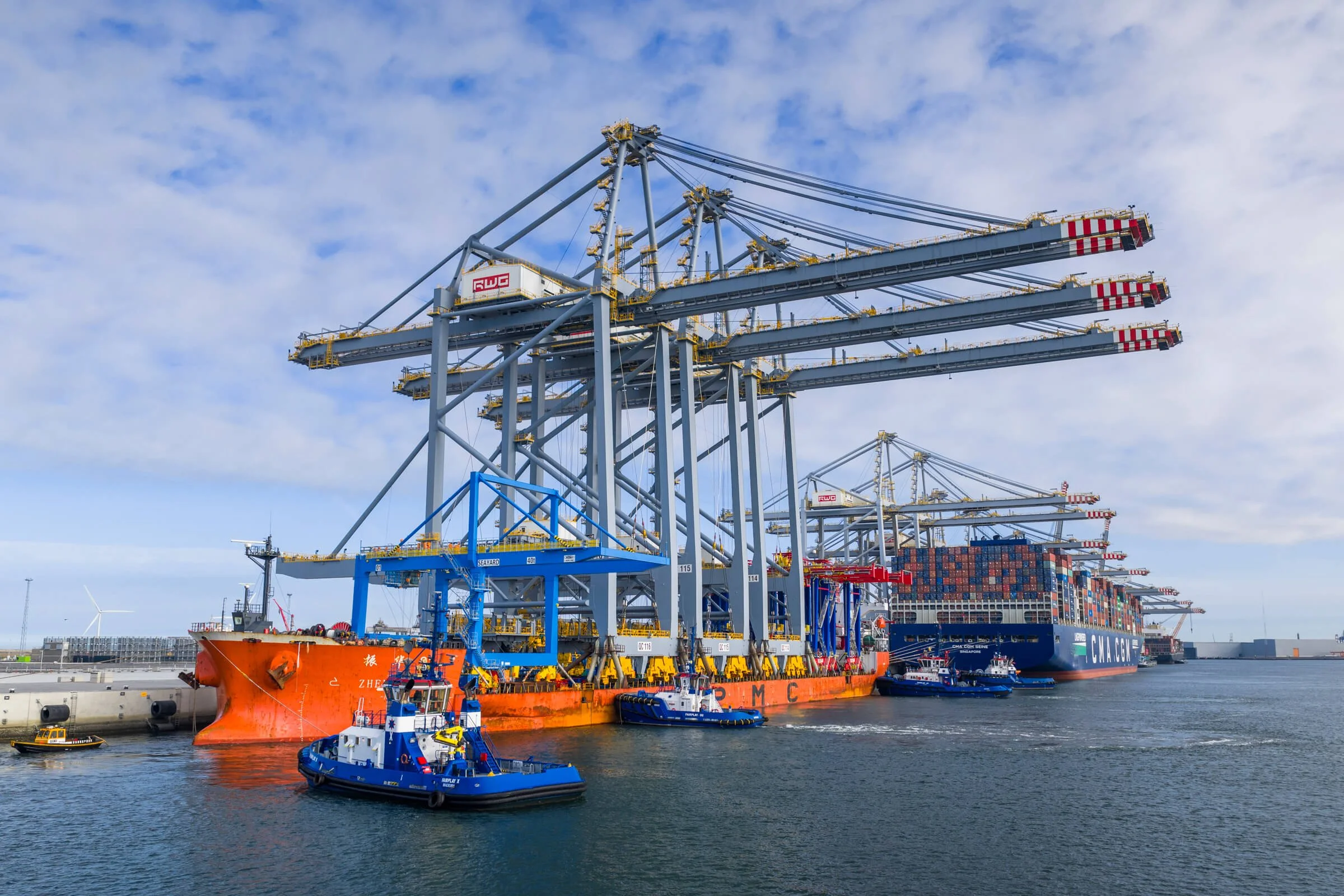 large container ship docked at port with cargo cranes and tugboats in water