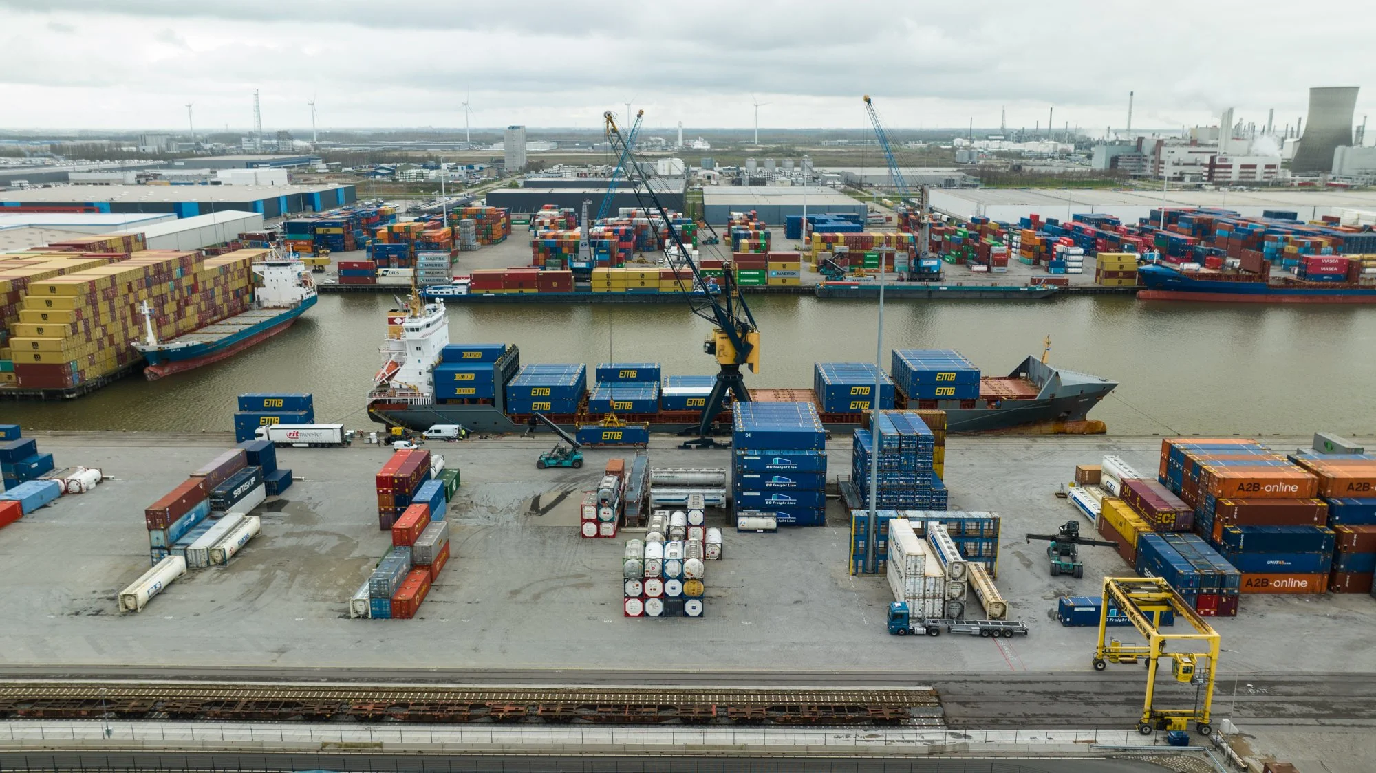 A busy shipping port with cargo ships, containers, cranes, and trucks for loading and unloading goods.