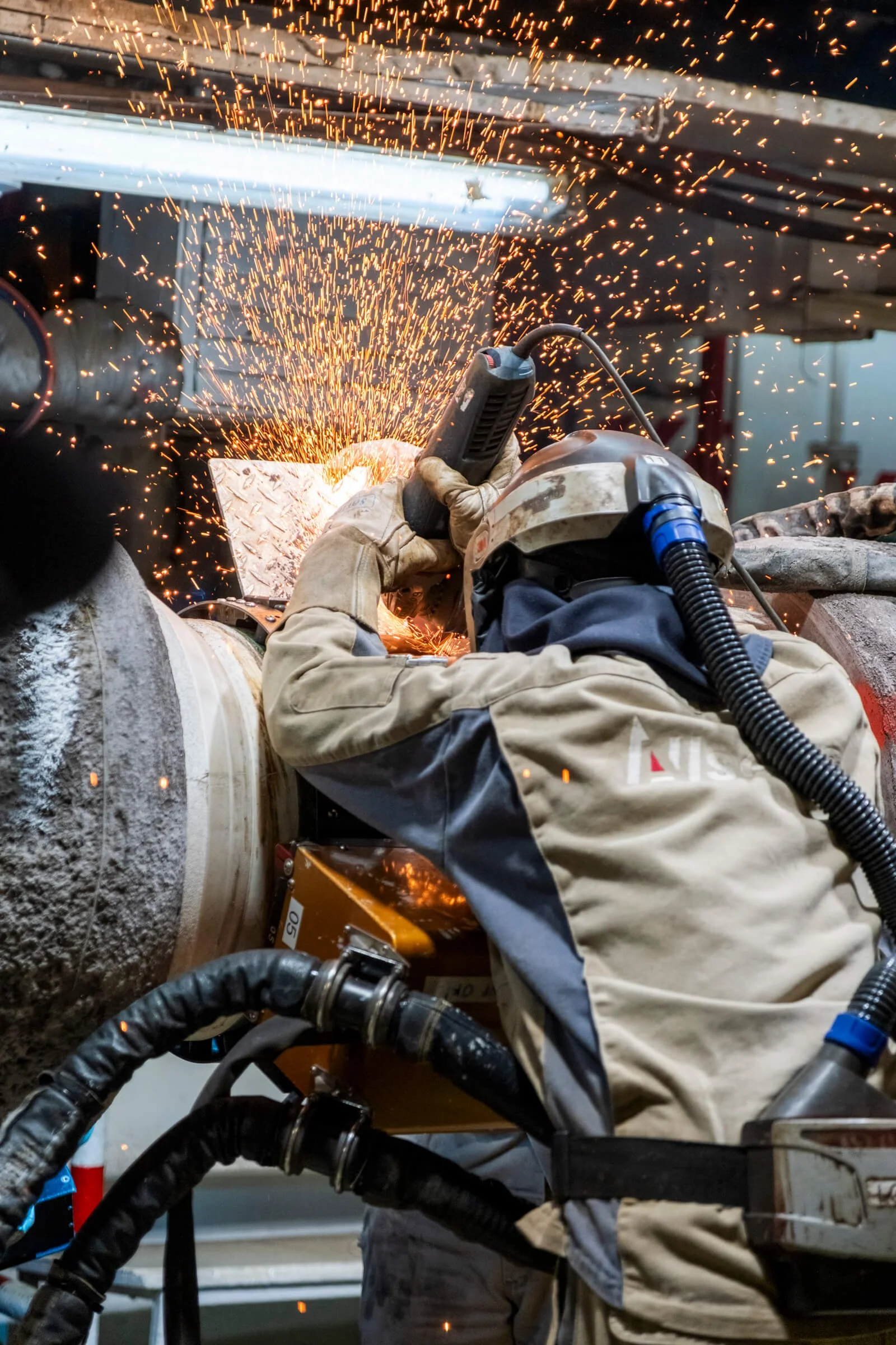 A worker welding metal with sparks flying in an industrial setting, wearing protective gear including a helmet and gloves.