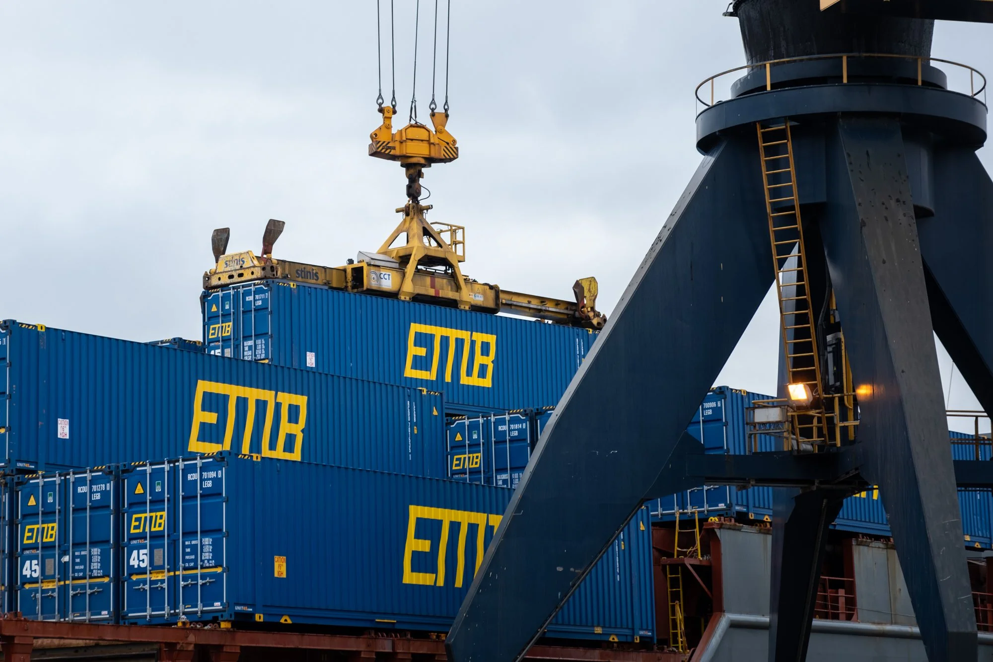 Shipping containers with the EMR logo stacked on a cargo ship, with a crane in the process of moving a container.