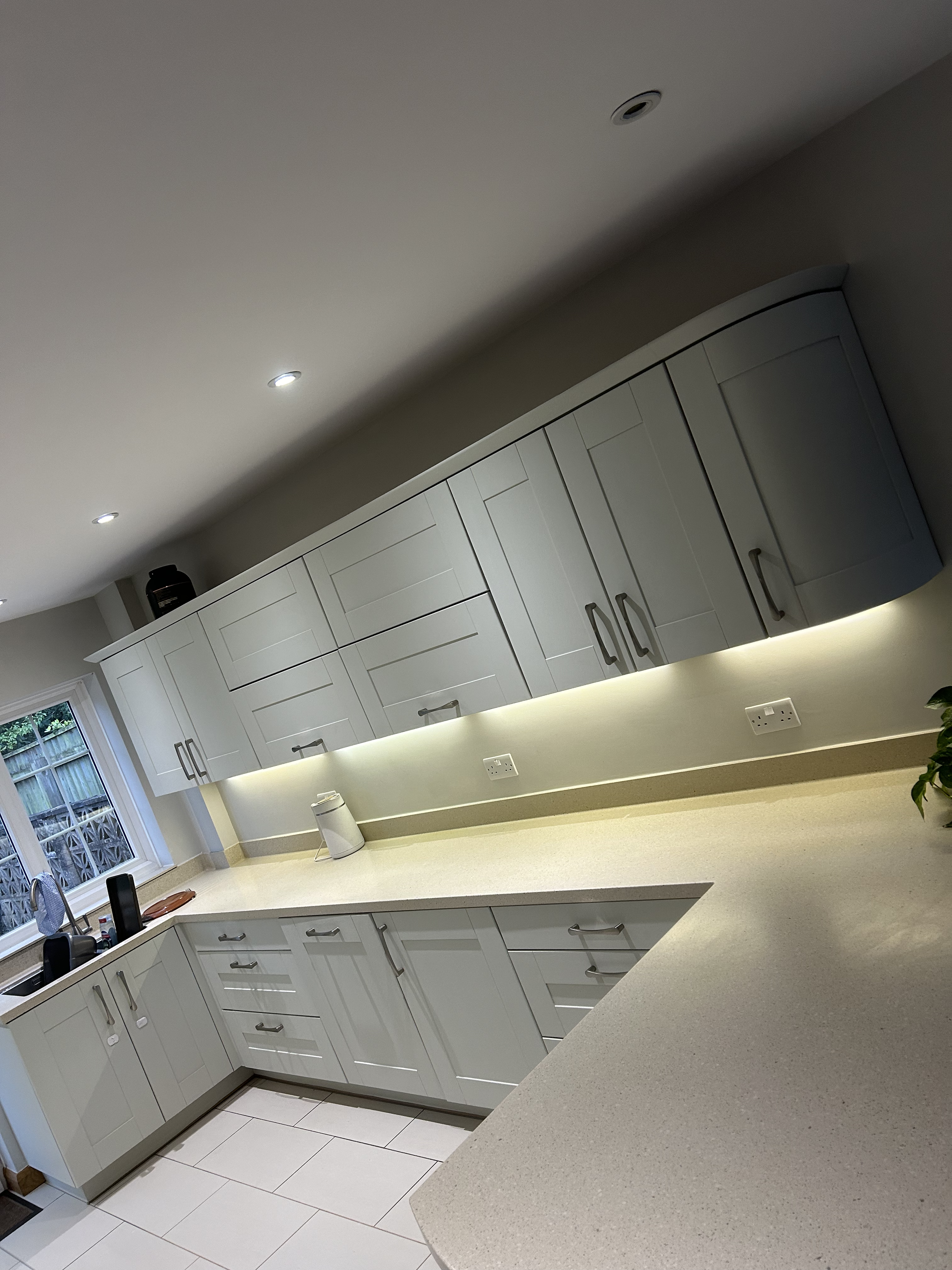 Modern kitchen with white cabinets, a beige countertop, a window, and under-cabinet lighting.