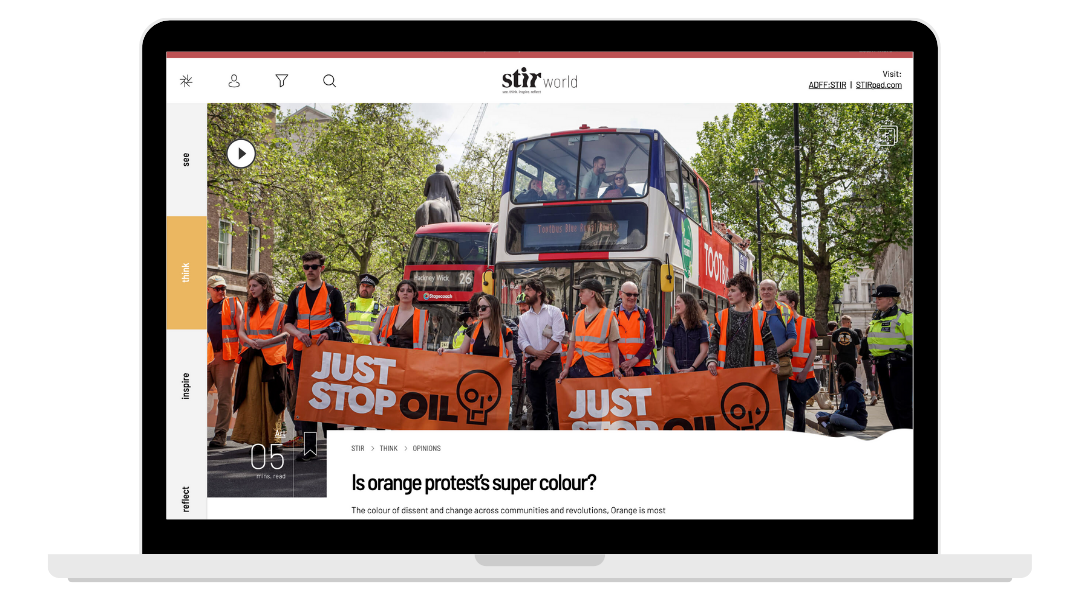 People protesting with orange banners that say "Just Stop Oil" on a street with a double-decker bus and trees in the background.