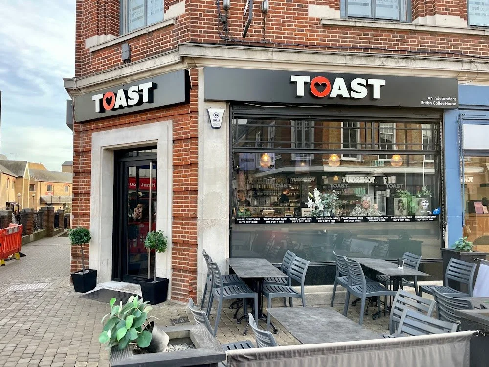 Exterior of a coffee shop named 'TOAST' on a corner street, with outdoor seating and potted plants outside.