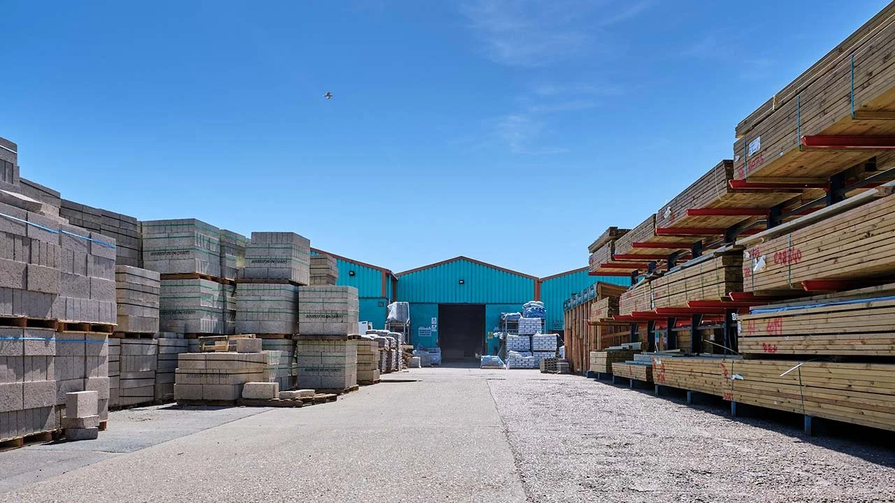 Outdoor lumber yard with stacks of wood and concrete blocks under a clear blue sky.