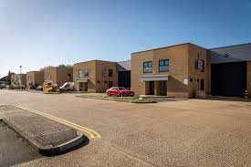 A row of small commercial or office buildings with brick exteriors on a sunny day. There are cars parked in front and a clear blue sky overhead.