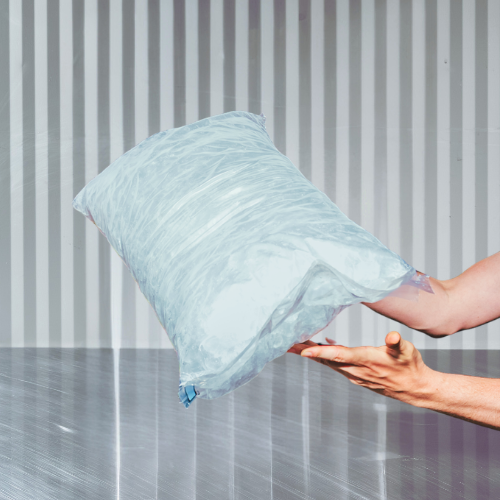 A hand holding an ice bag with a background of vertical metallic bars and a stainless table, with an overlay text "Coming Summer 2026".
