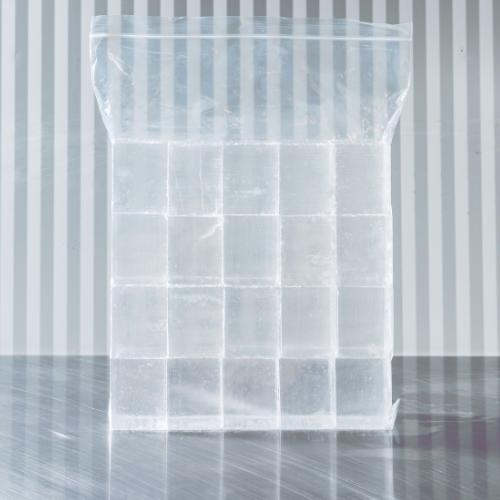 A clear plastic bag filled with large ice cubes on a gray surface with a striped gray and white background.