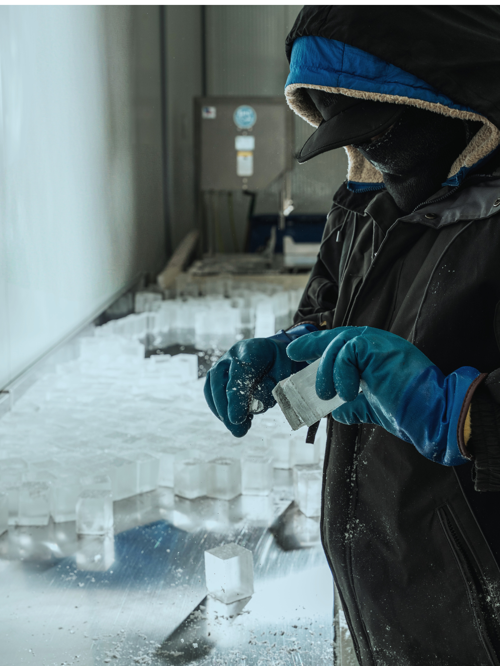 Person in winter clothing and gloves working with ice blocks in a refrigerated environment.