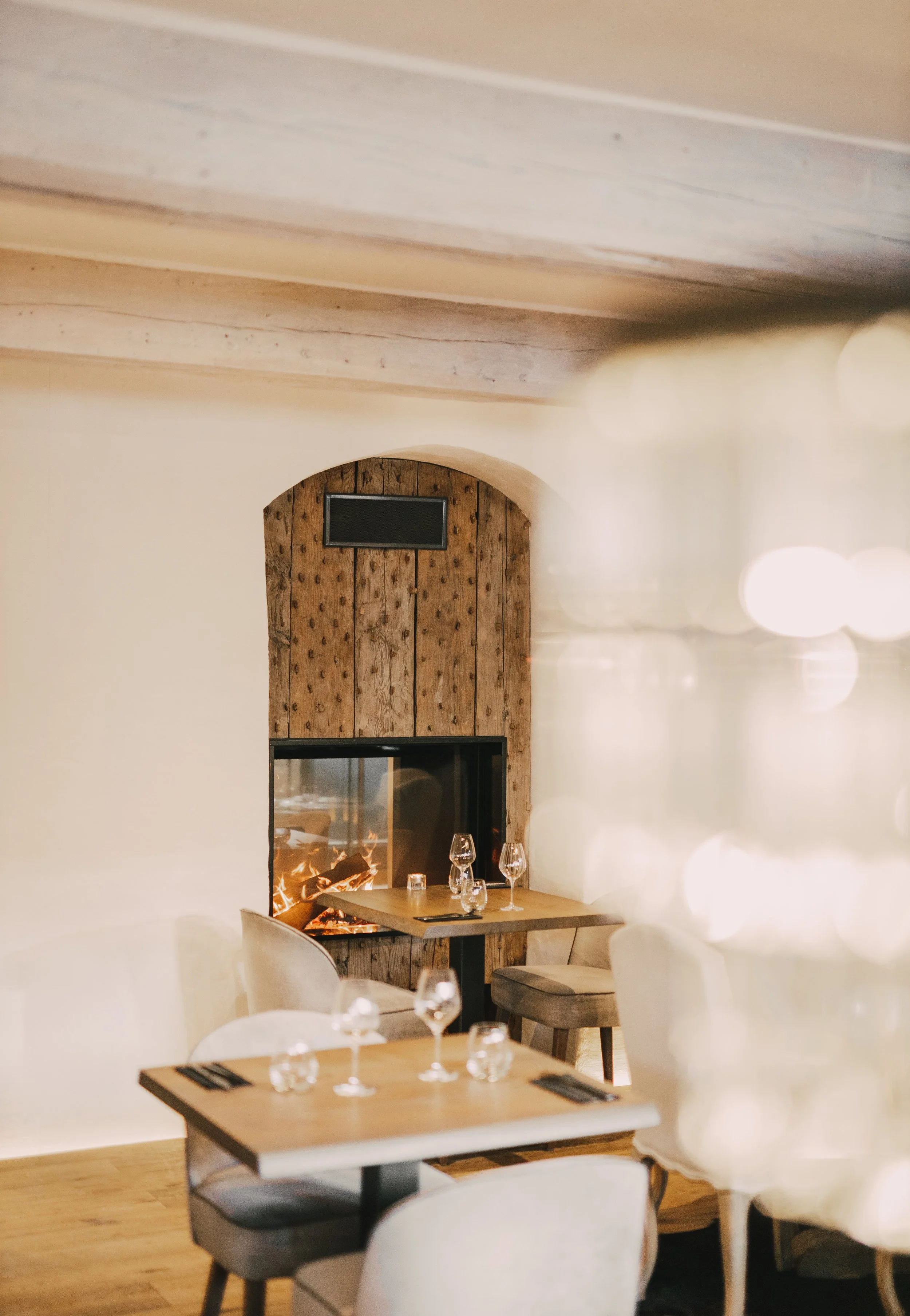 A cozy restaurant interior with wooden tables, chairs, and a fireplace, decorated in warm tones.