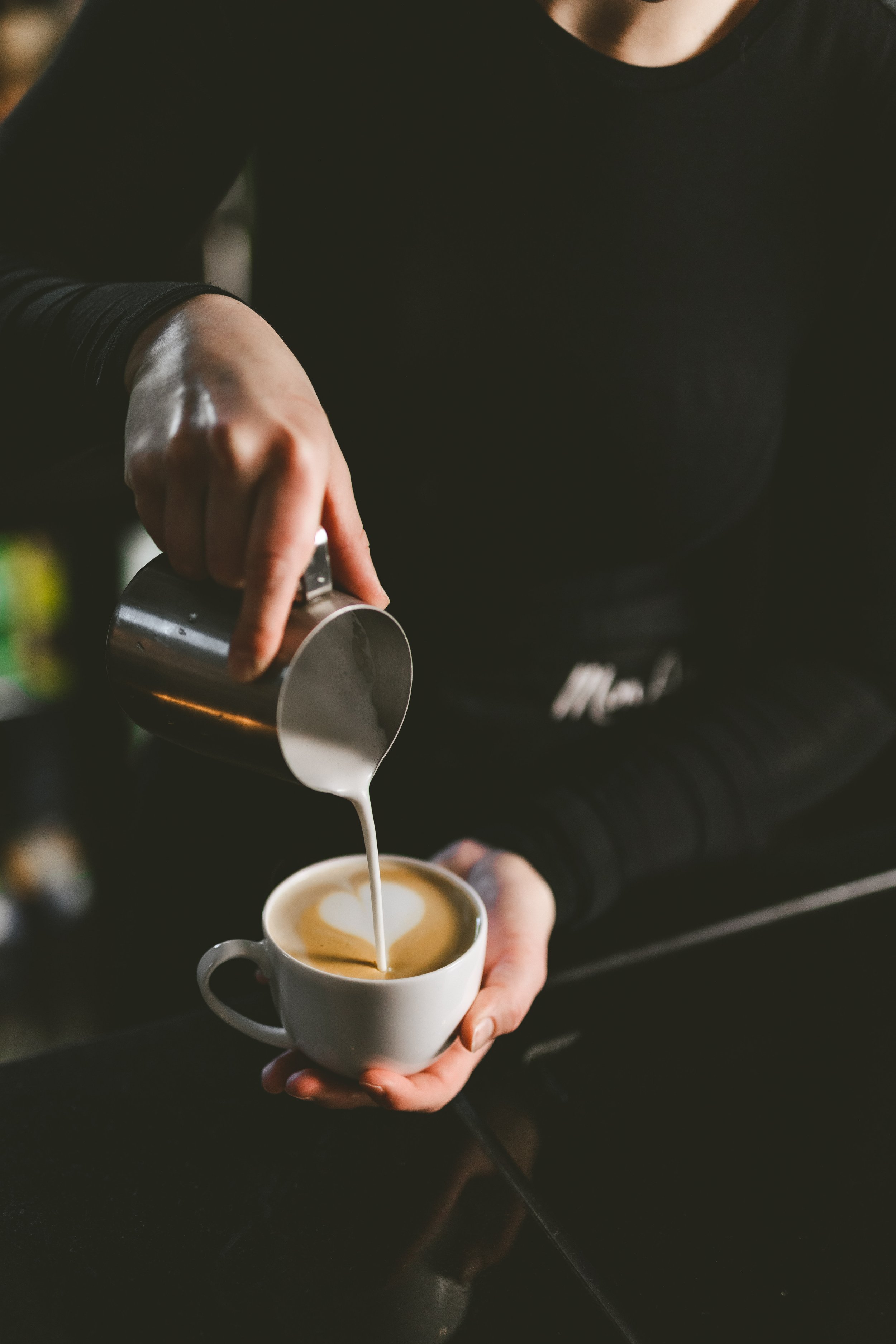 Person pouring steamed milk into a cup of coffee to create latte art.