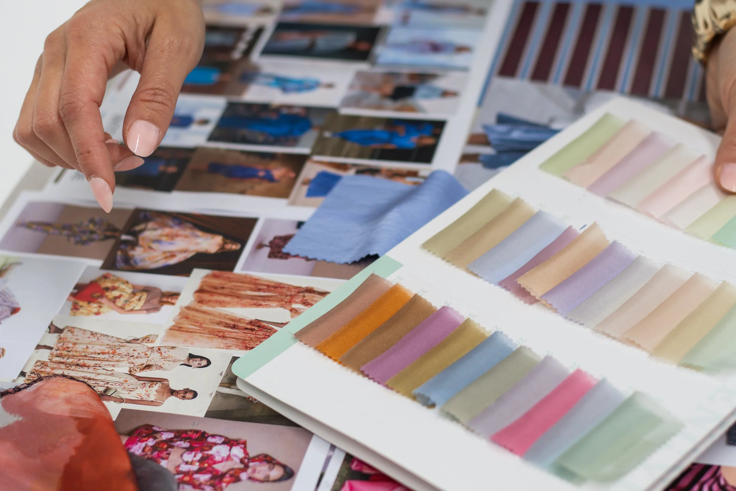 Person comparing fabric swatches to photos of models in fashion magazine.