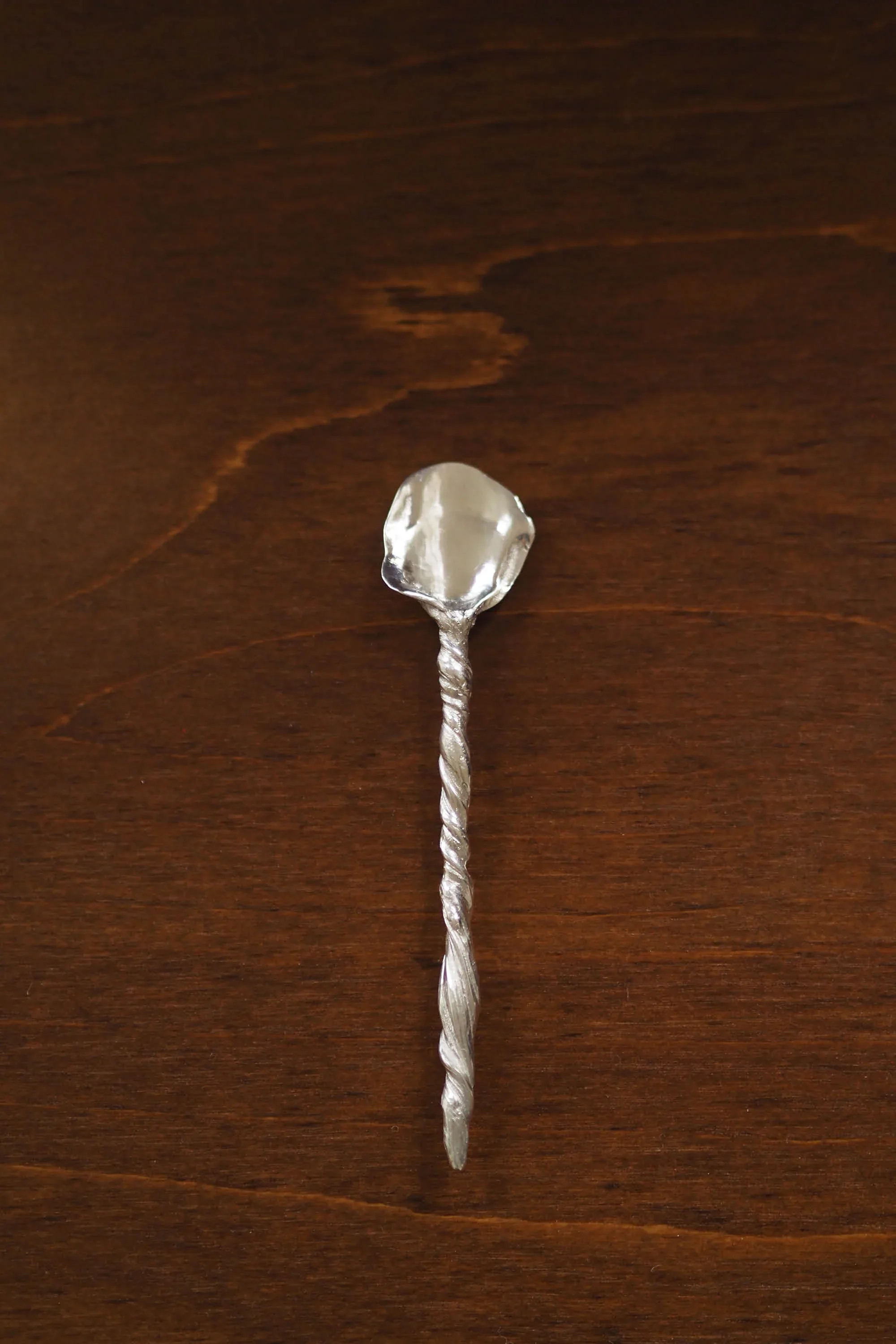 A silver spoon with a twisted handle placed on a wooden surface.