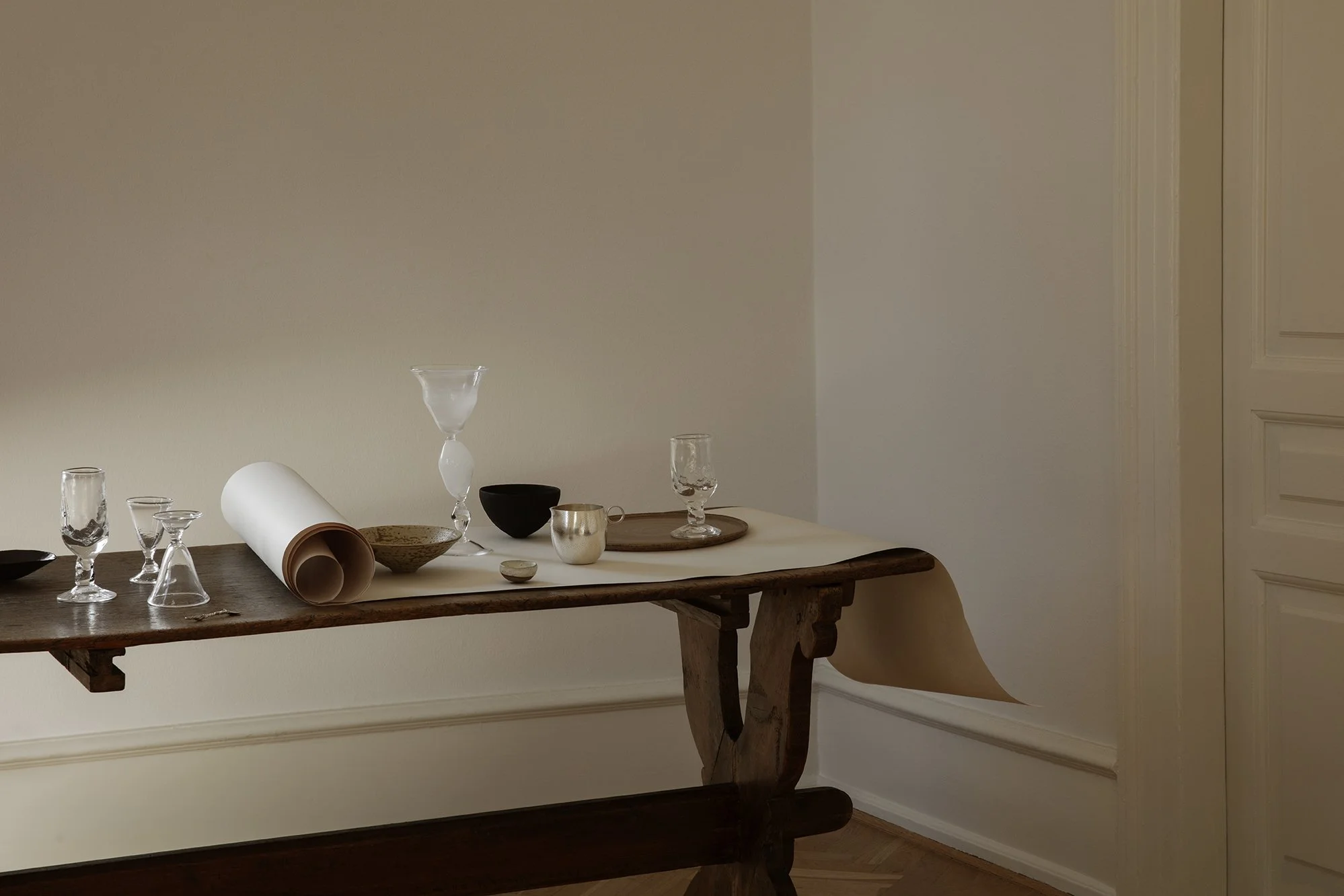 A wooden table with glassware, bowls, and paper rolls against a beige wall.