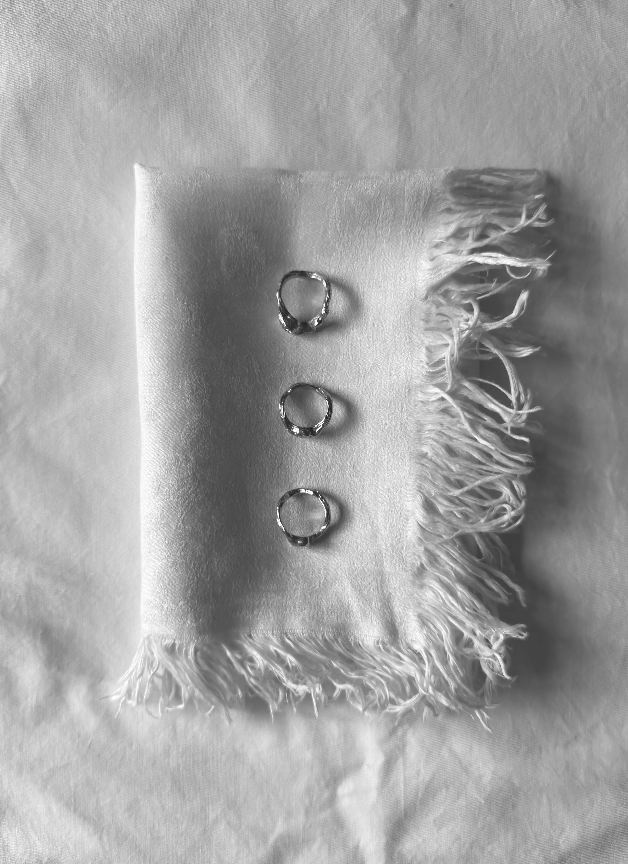 Three rings on a piece of cloth with frayed edges, arranged vertically in the center of the image.
