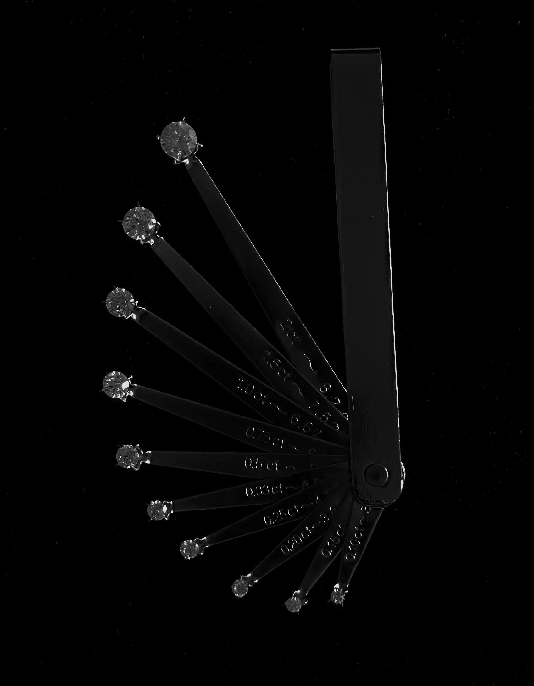 A metallic graduated ruler with a diamond mounted on the end, fanned out in a semicircular pattern against a black background.