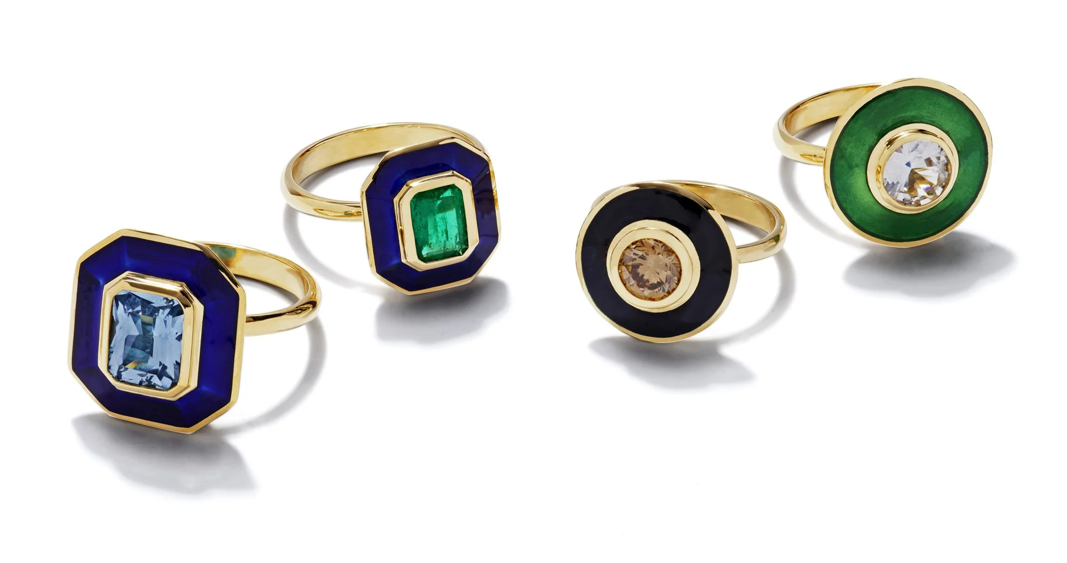 Four gold rings with large colorful gemstone centers, two rings with blue and green stones and two rings with black and green enamel accents featuring clear central gemstones.