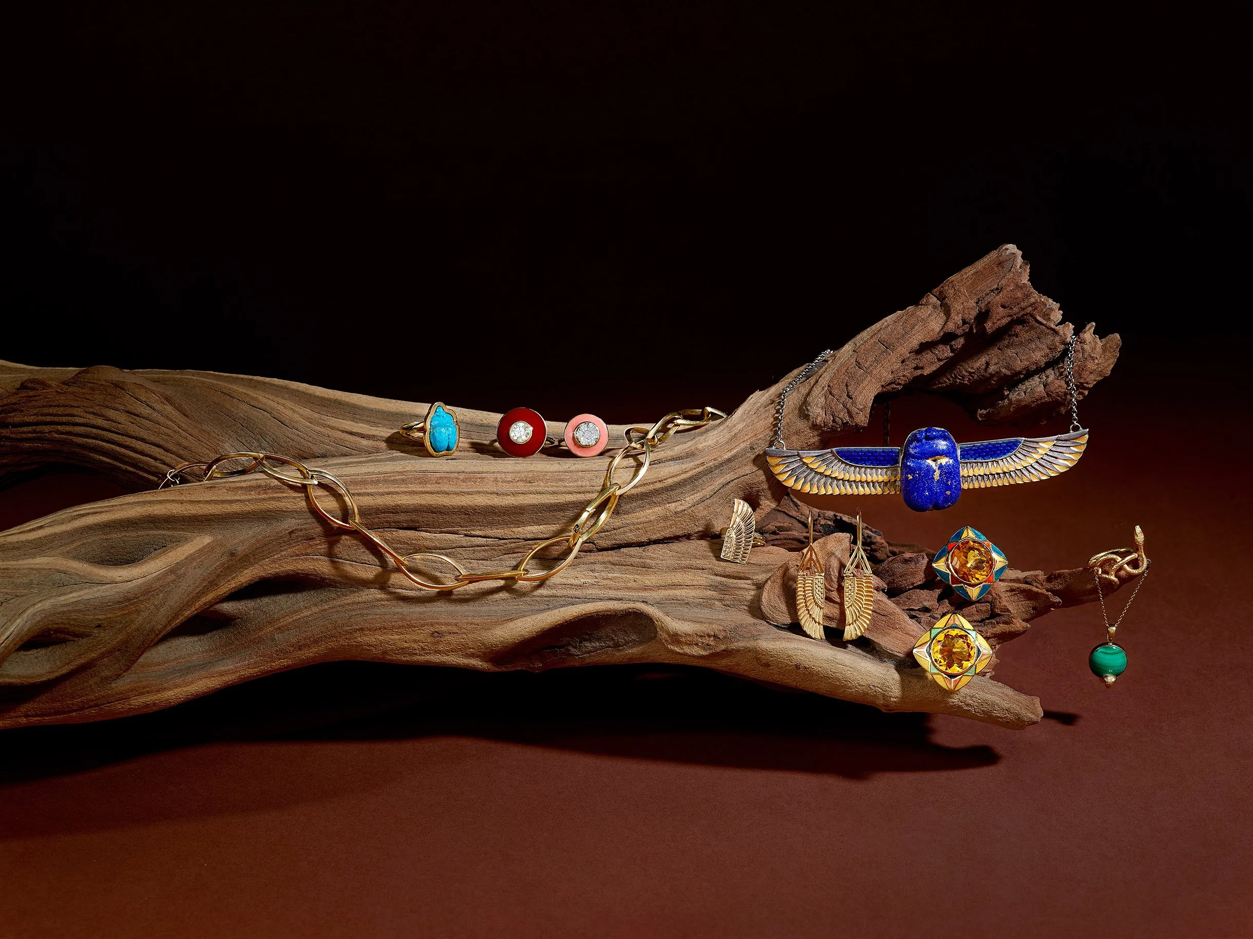 Jewelry including earrings, rings, necklaces, and bracelets displayed on a twisted piece of wood, featuring colorful stones and gold accents.