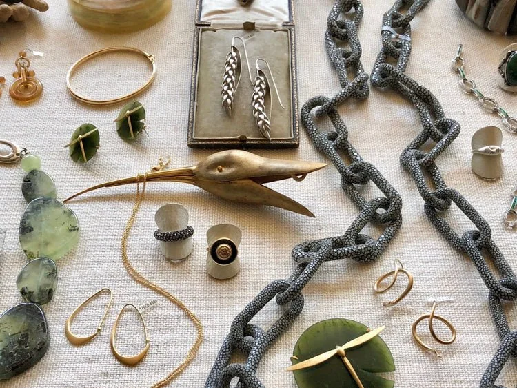 Jewelry display with various accessories including earrings, necklaces, rings, and a decorative gold bird sculpture on a beige fabric background.