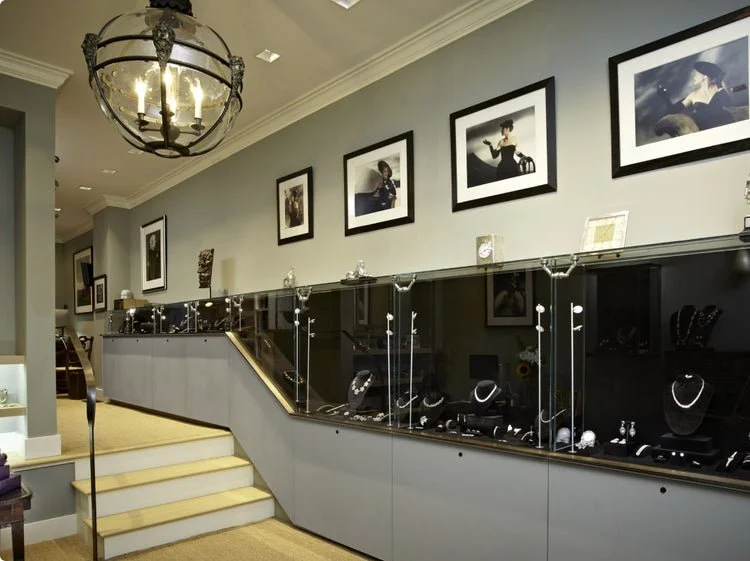 Jewelry display case with necklaces and earrings, framed photos on the wall, chandelier lighting, stairs leading up to the display, and decorative items on top of the case.