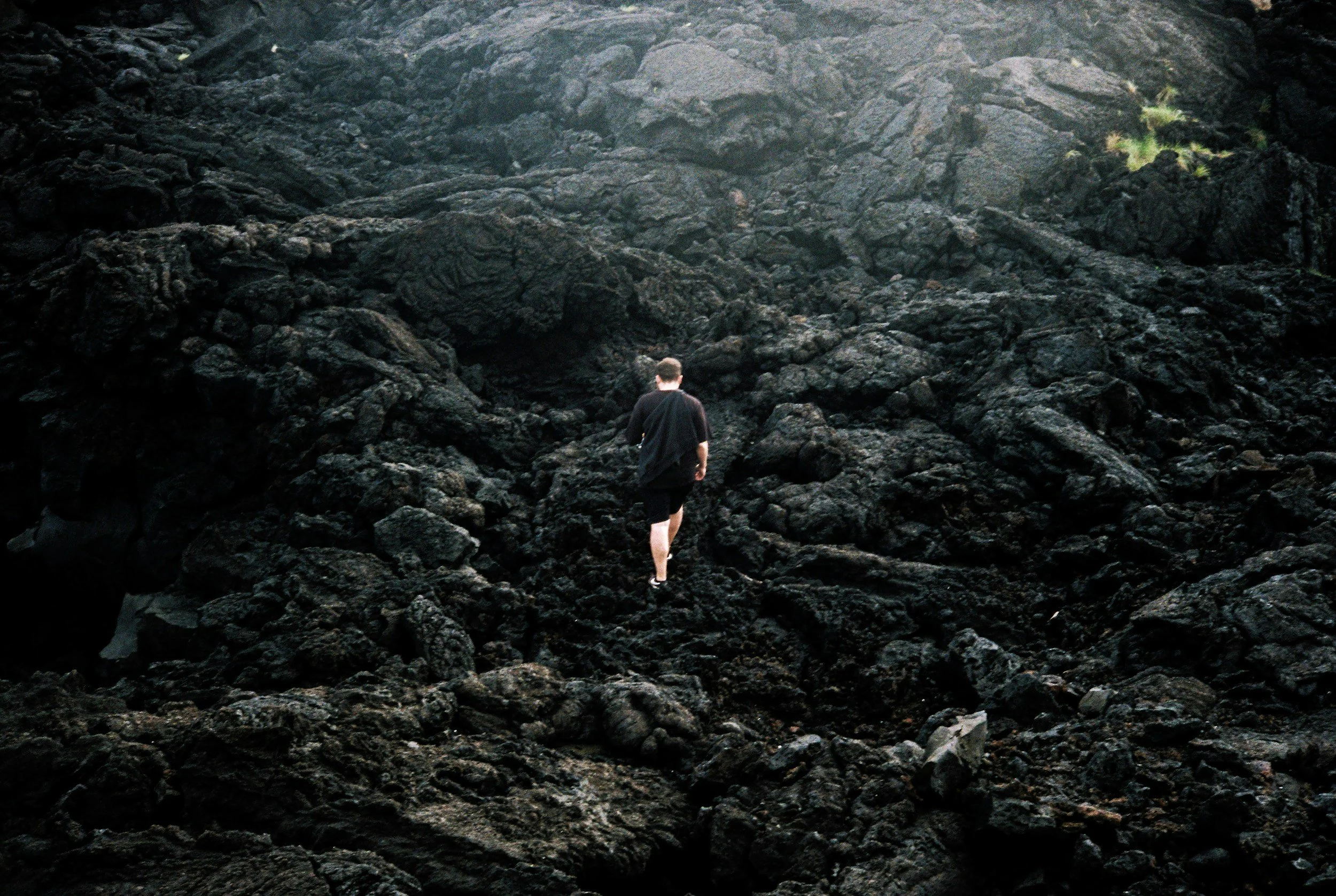 A person walking across a landscape of dark volcanic rocks.