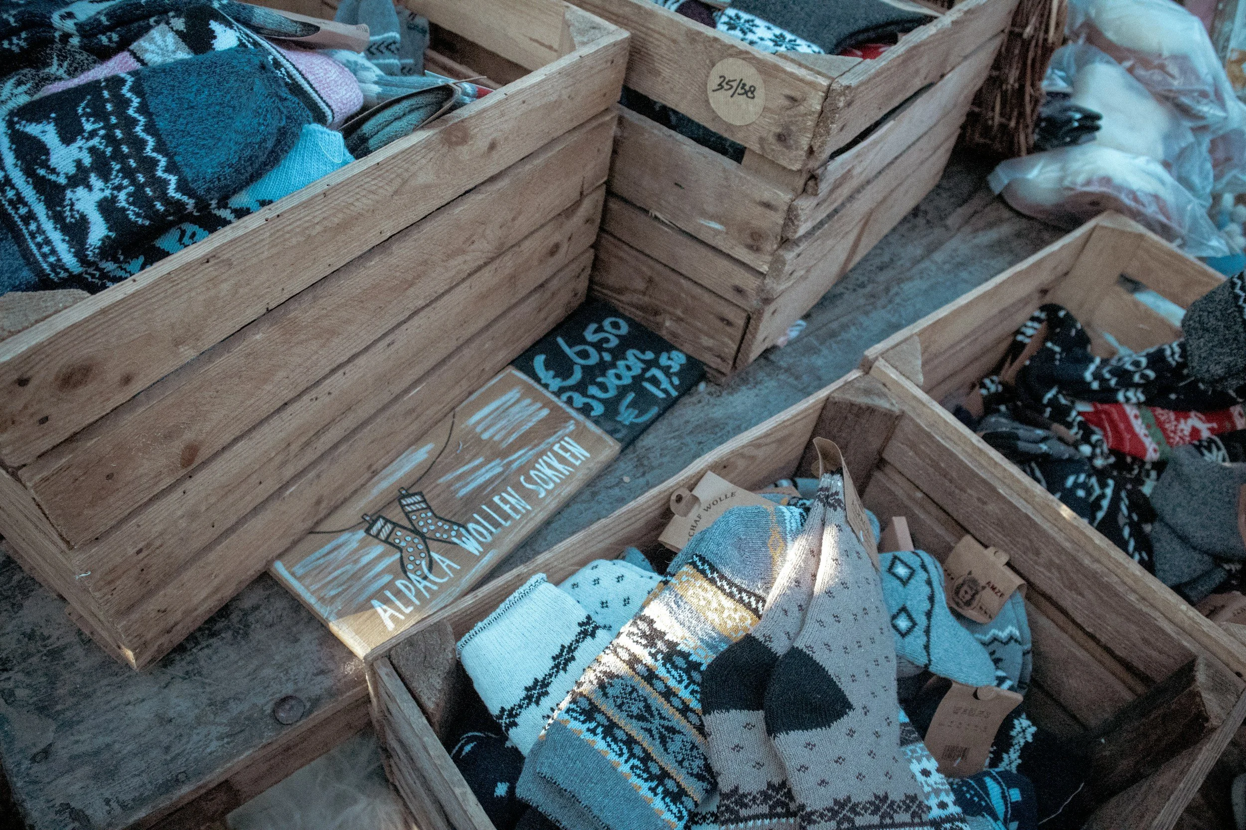 Multiple wooden crates filled with assorted socks, some featuring holiday or winter patterns, displayed at a retail store.
