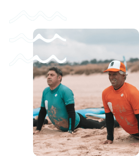 Time to Surf founder and instructor on the beach with learner. Two people in wetsuits practicing yoga on a sandy beach with surfboards, under a cloudy sky.