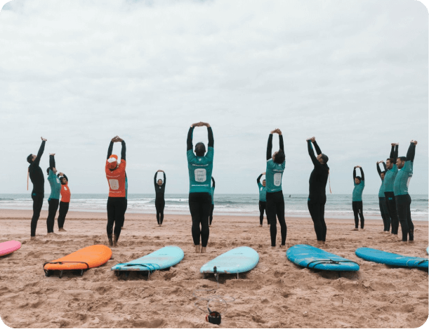 People practicing yoga on the beach at Time to Surf yoga lesson with surfboards in the foreground and the ocean in the background.