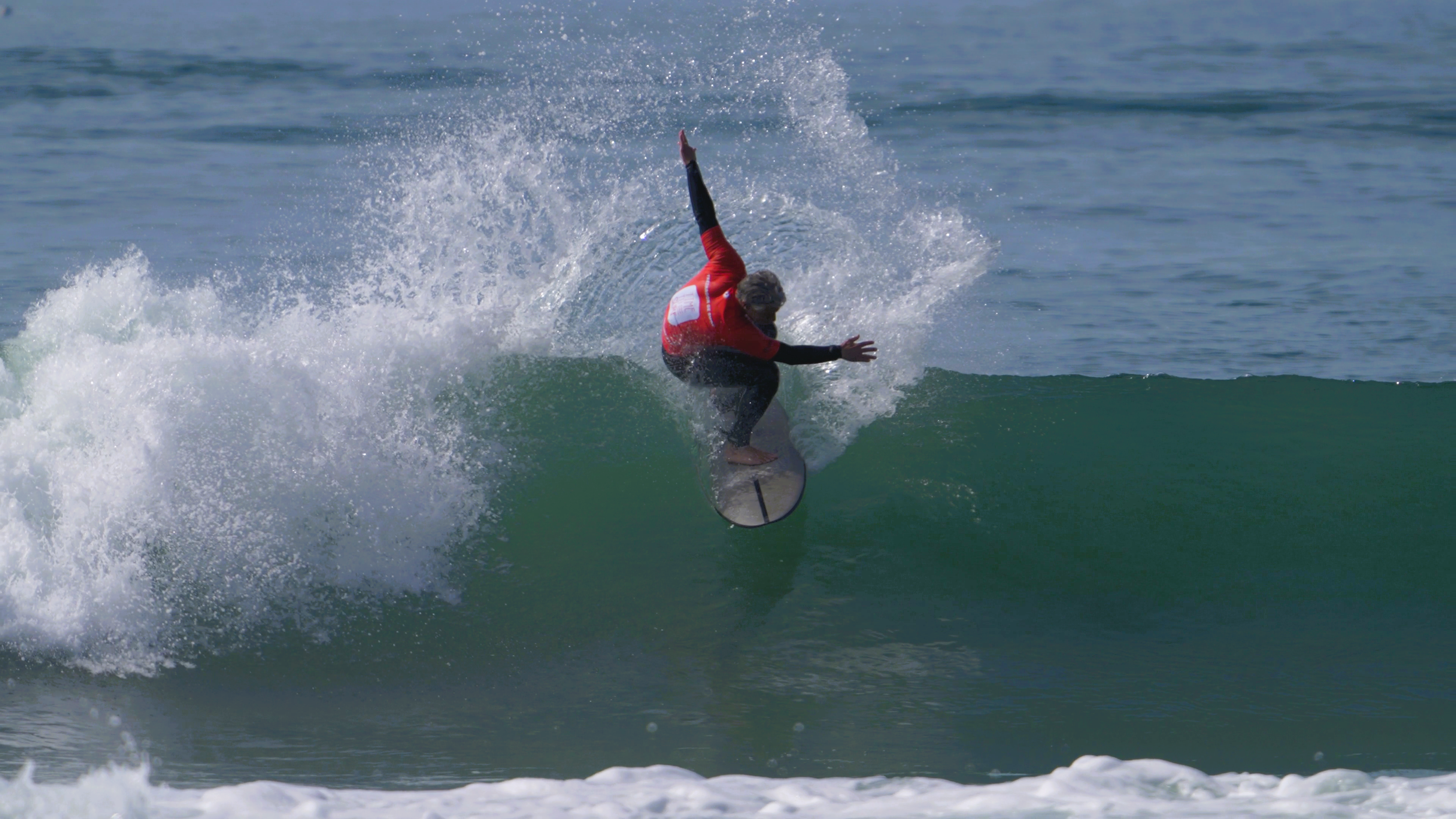 Person surfing a wave at the beach with a person in a red wetsuit riding a surfboard.