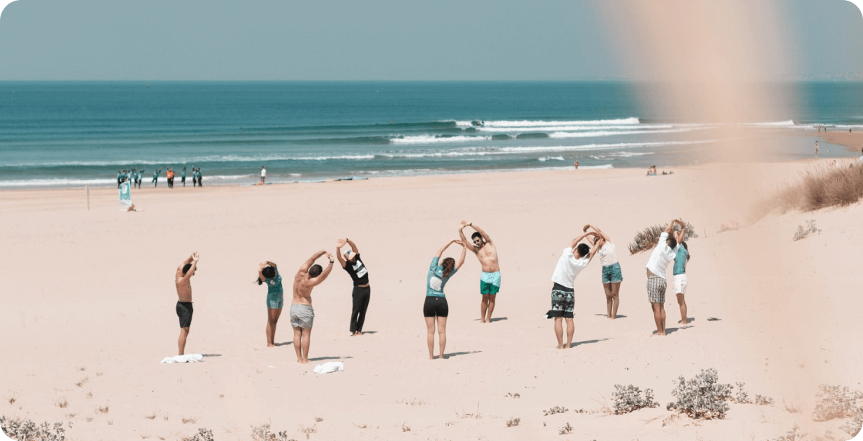 Group of people practicing yoga at a Time to Surf beach yoga session, on a sandy beach with ocean waves in the background.