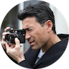 Time to Surf review profile image - A person with dark hair holding a camera, focusing on taking a photo.