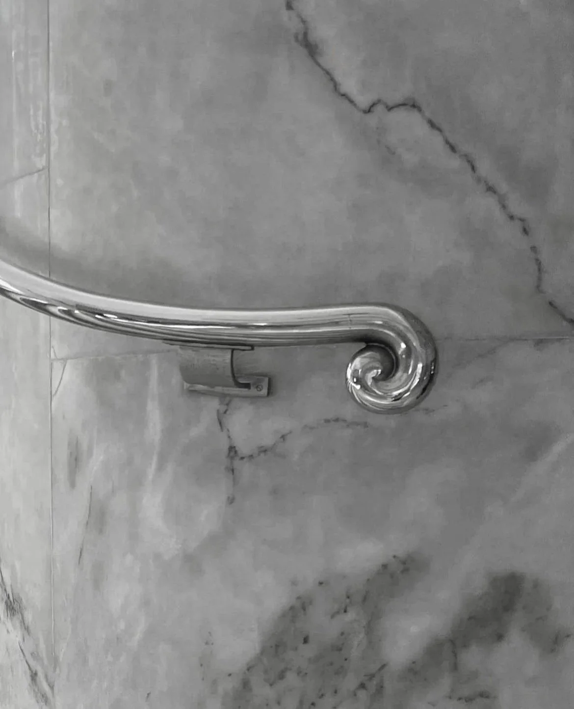 Ein silberner Handlauf mit spiralförmigem Ende an einer Marmorwand.