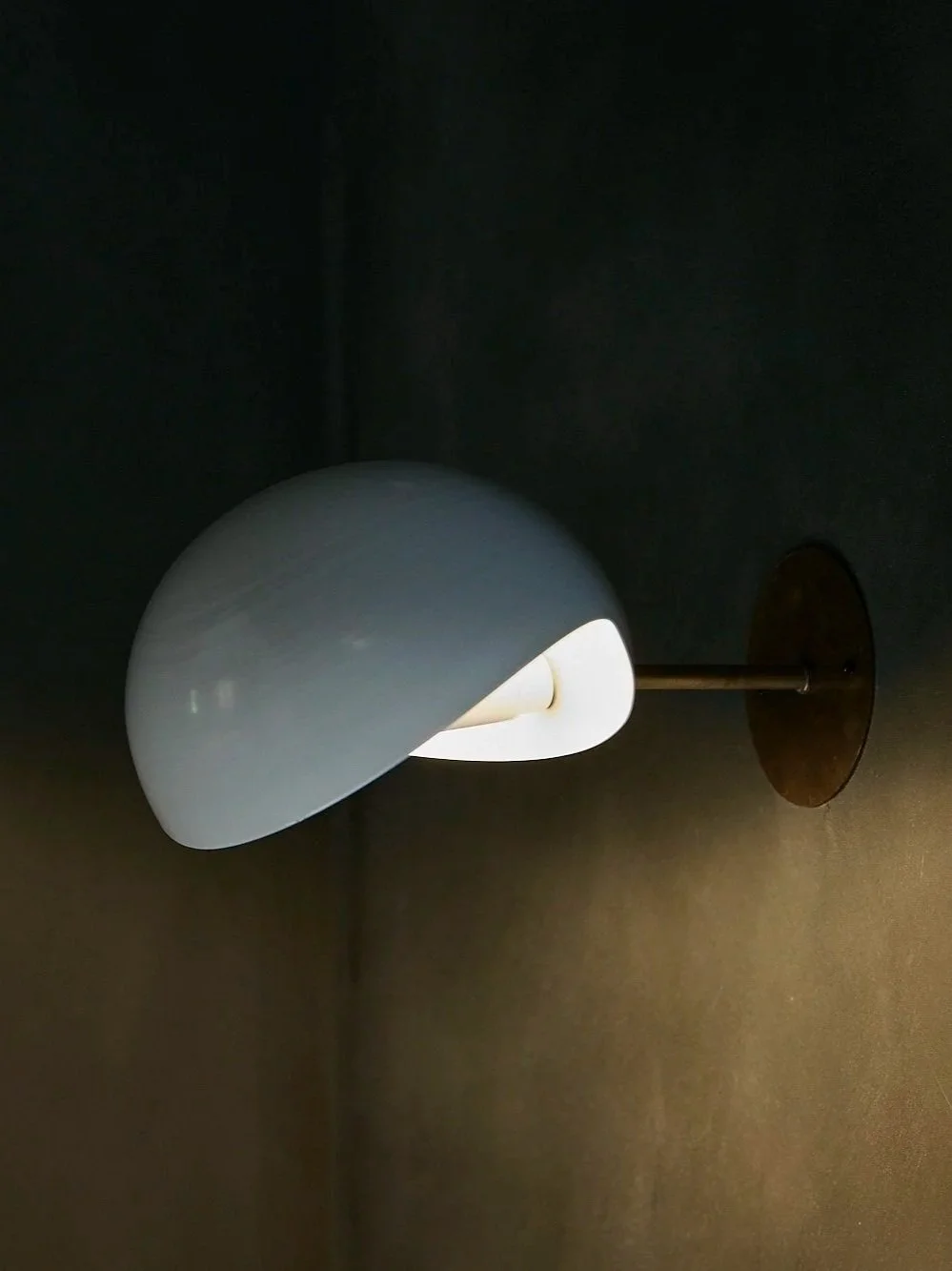 Wandlampe mit halb abgedecktem weißen Schirm an einer schwarzen Wand.