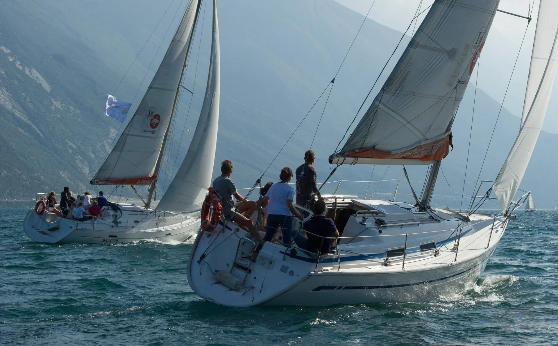 Two sailboats racing on the water with crews onboard and mountains in the background