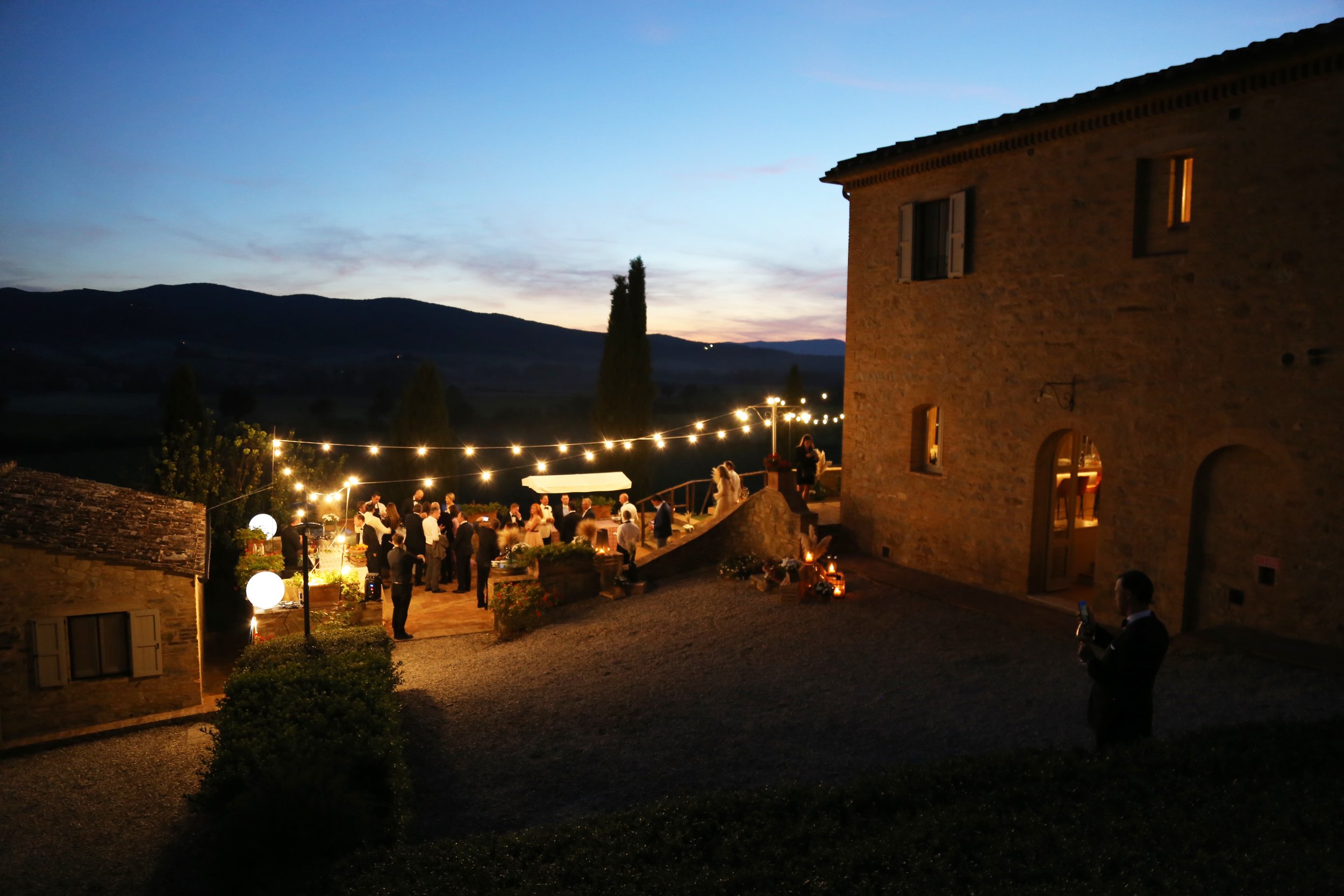 A group of friends enjoying a hot spring with waterfalls and natural surroundings, some sitting and others socializing in the water.