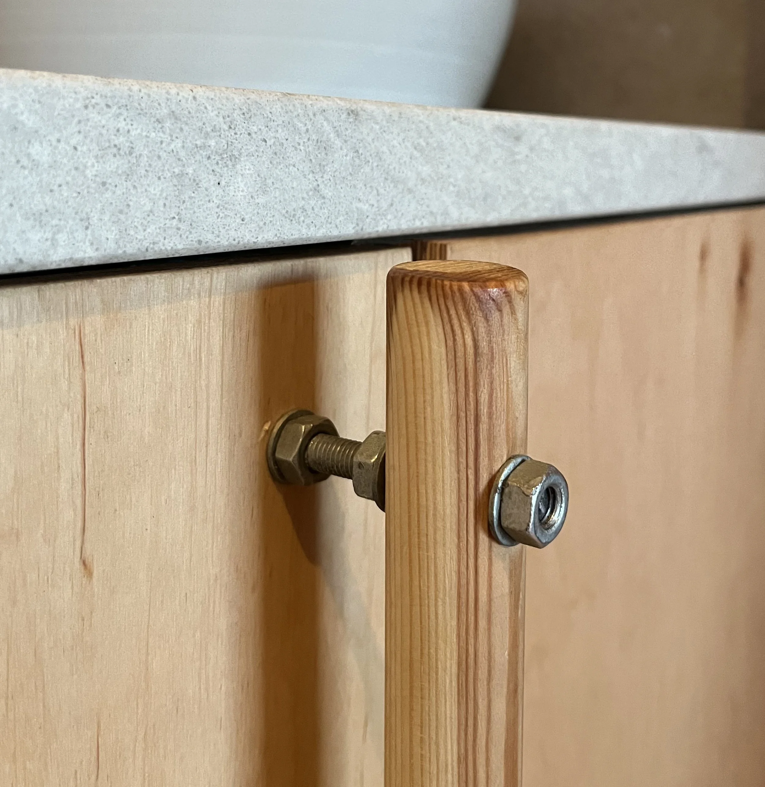 Close-up of a wooden cabinet door with hardware connecting it to the cabinet frame, with a light-colored wood finish and a grey countertop above it.