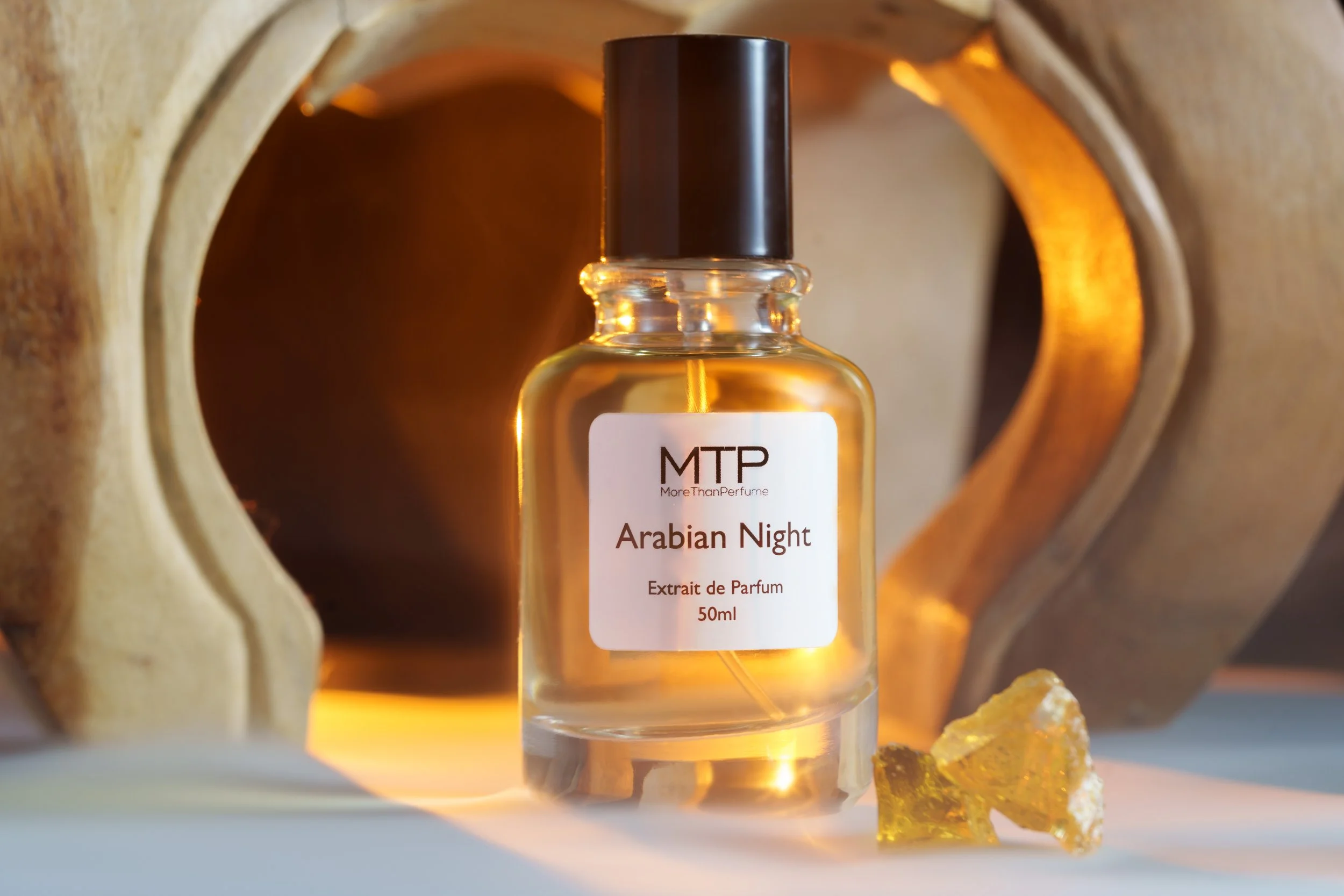 Flasche mit Parfüm namens Arabain Night, umgeben von warmem Licht und einem Stück Bernstein, im Hintergrund ein holzartiges Dekor.
