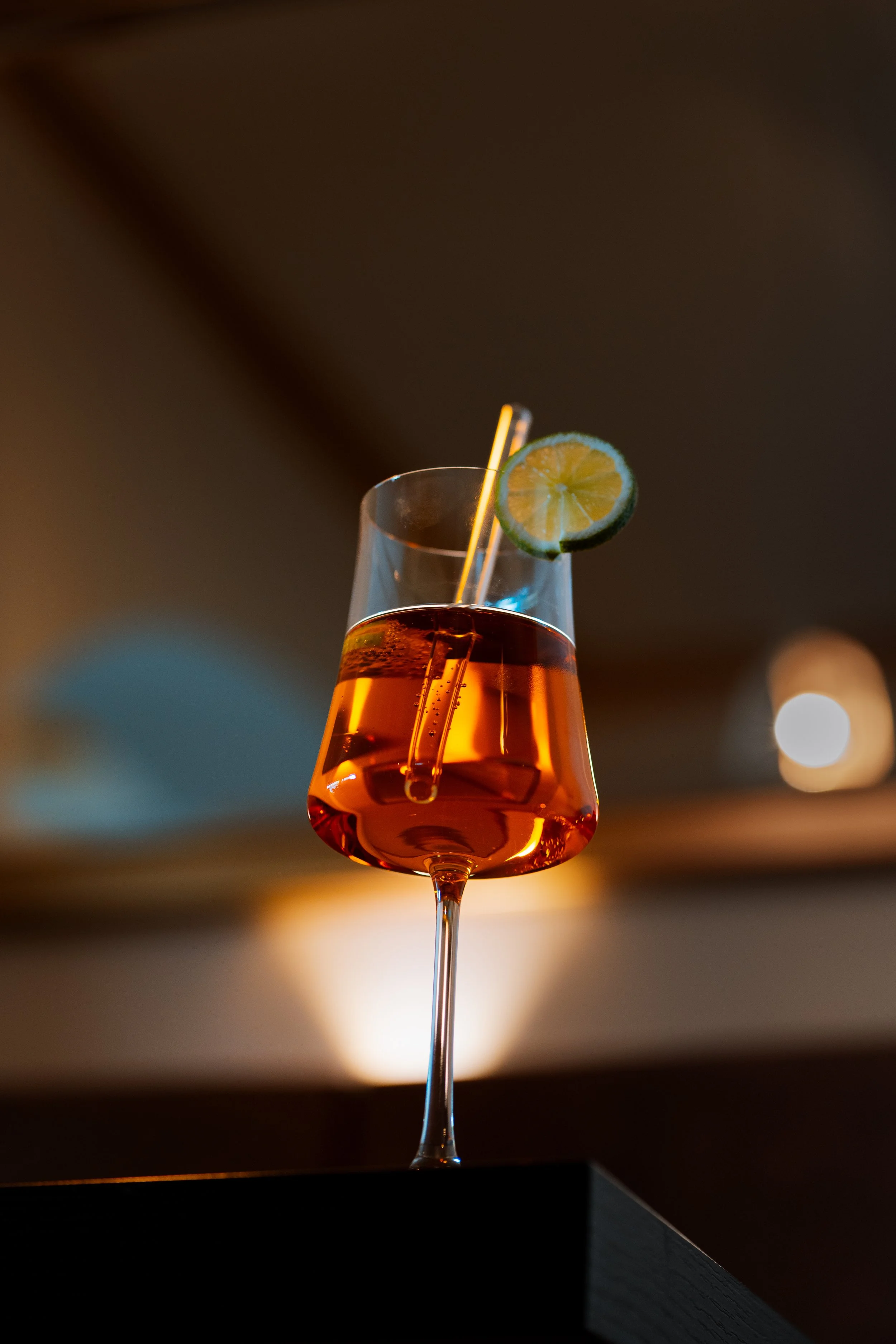 Cocktailglas mit bernsteinfarbener Flüssigkeit, Zitrusscheibe und Strohhalm bei gedämpftem Licht, Aperol Spritzt