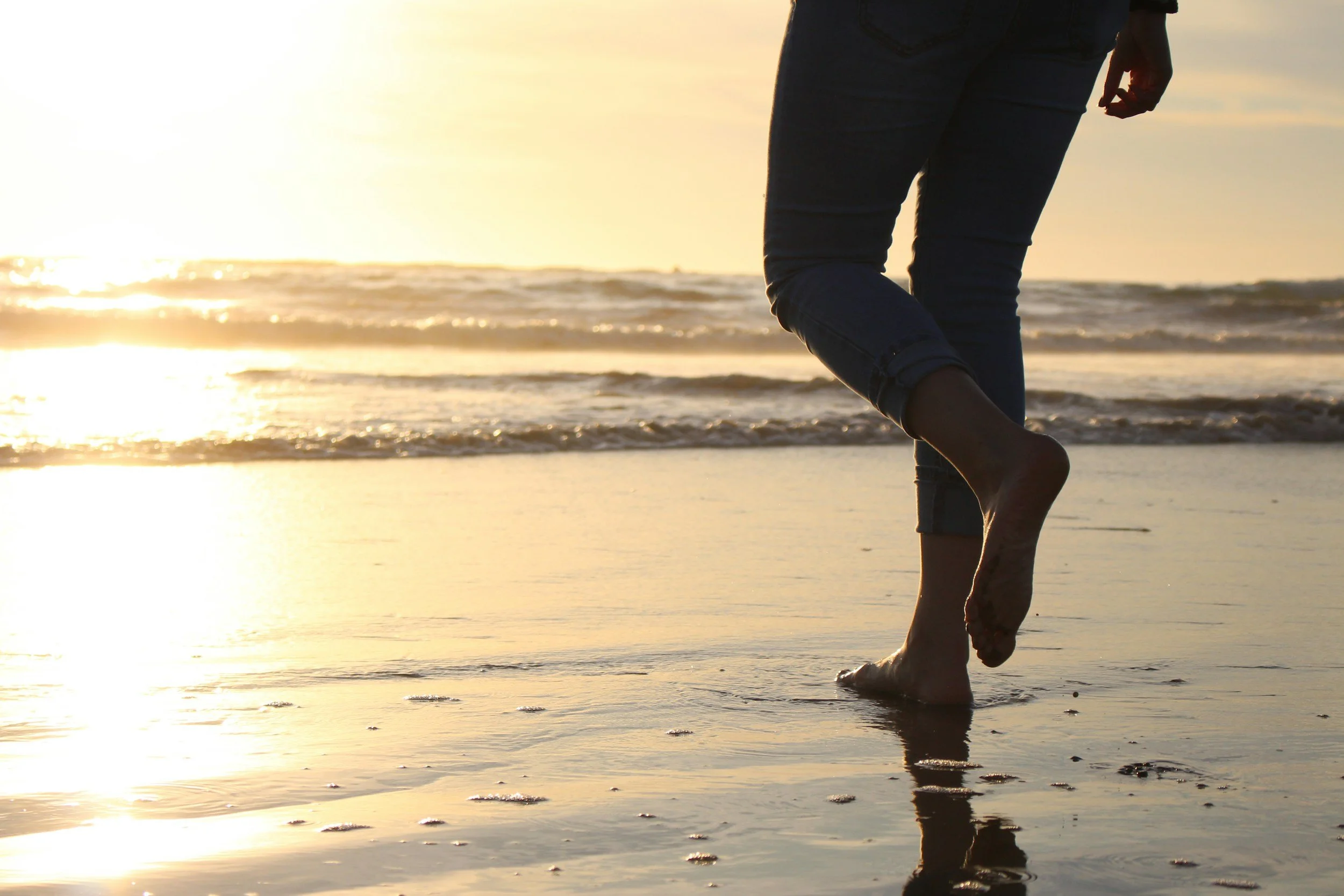 Person walking barefoot along the beach at sunset.  Pathwise Psychology in WA and OR.
