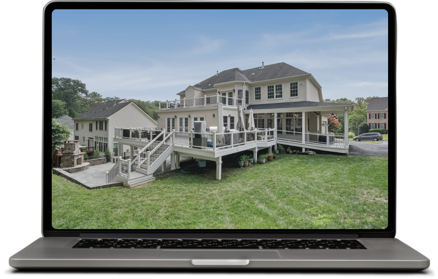 A large two-story house with beige siding, multiple decks, and stairs leading down to a grassy yard.
