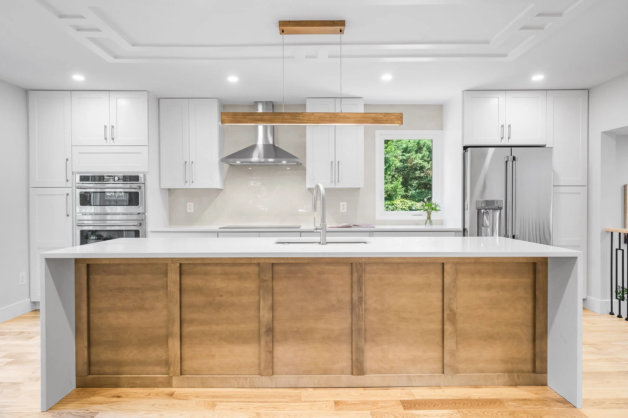Modern kitchen with white cabinets, stainless steel appliances, and a large island with a wooden base and white countertop.