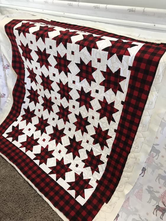 A Christmas quilt with red and black plaid star patterns, bordered by a red and black buffalo check pattern, draped over a surface.