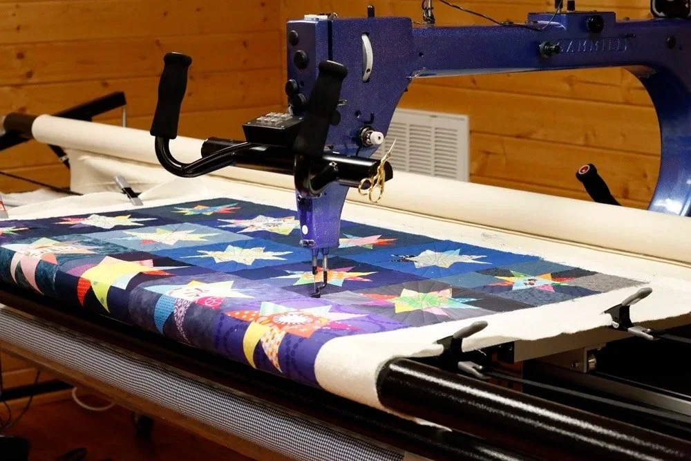 A machine quilting a colorful quilt featuring star and holly leaf patterns.