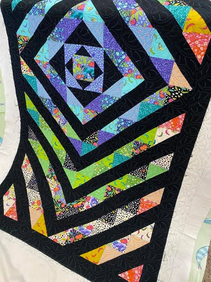 A colorful spiral quilt with black borders and various vibrant patterned fabric triangles.