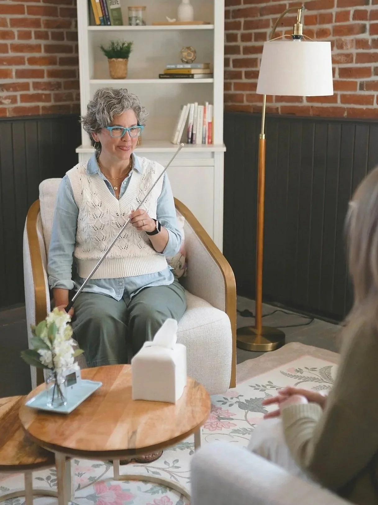 Kathleen Peters holding a brainspotting pointer during a therapy session, seated across from a client in a cozy, brick-walled office.