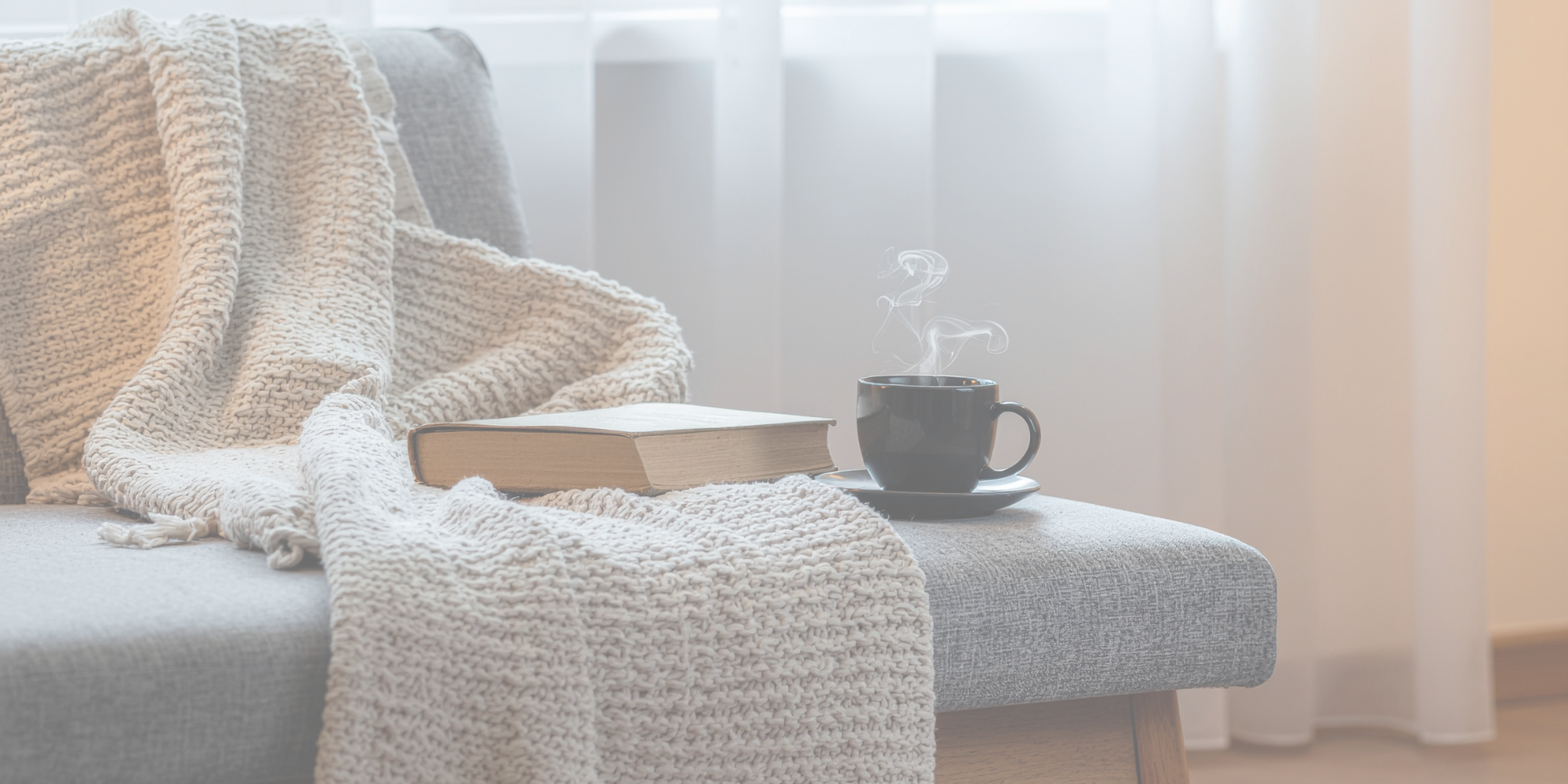 Couch holding blanket, book, and steaming hot beverage