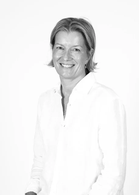 Black and white photo of a smiling middle-aged woman with short hair, wearing a white button-up shirt, against a plain background.