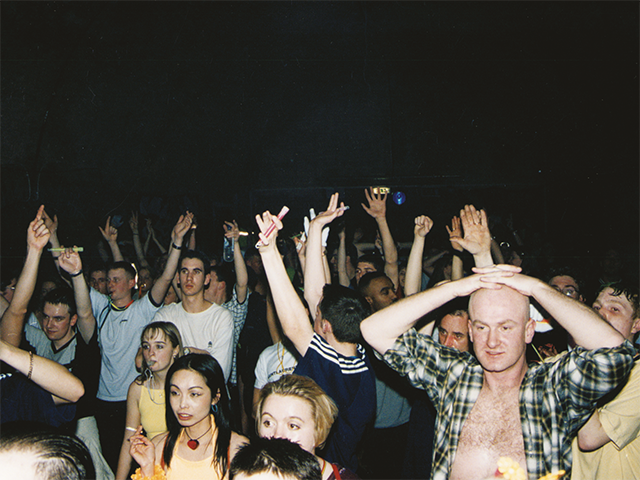 Crowd dancing at UK rave event with hands raised beneath club lighting